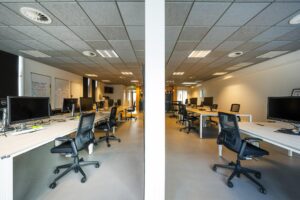 Moderne en ruime kantoorruimte aan de De Ruijterkade met werkplekken en computerschermen aan lange bureaus.